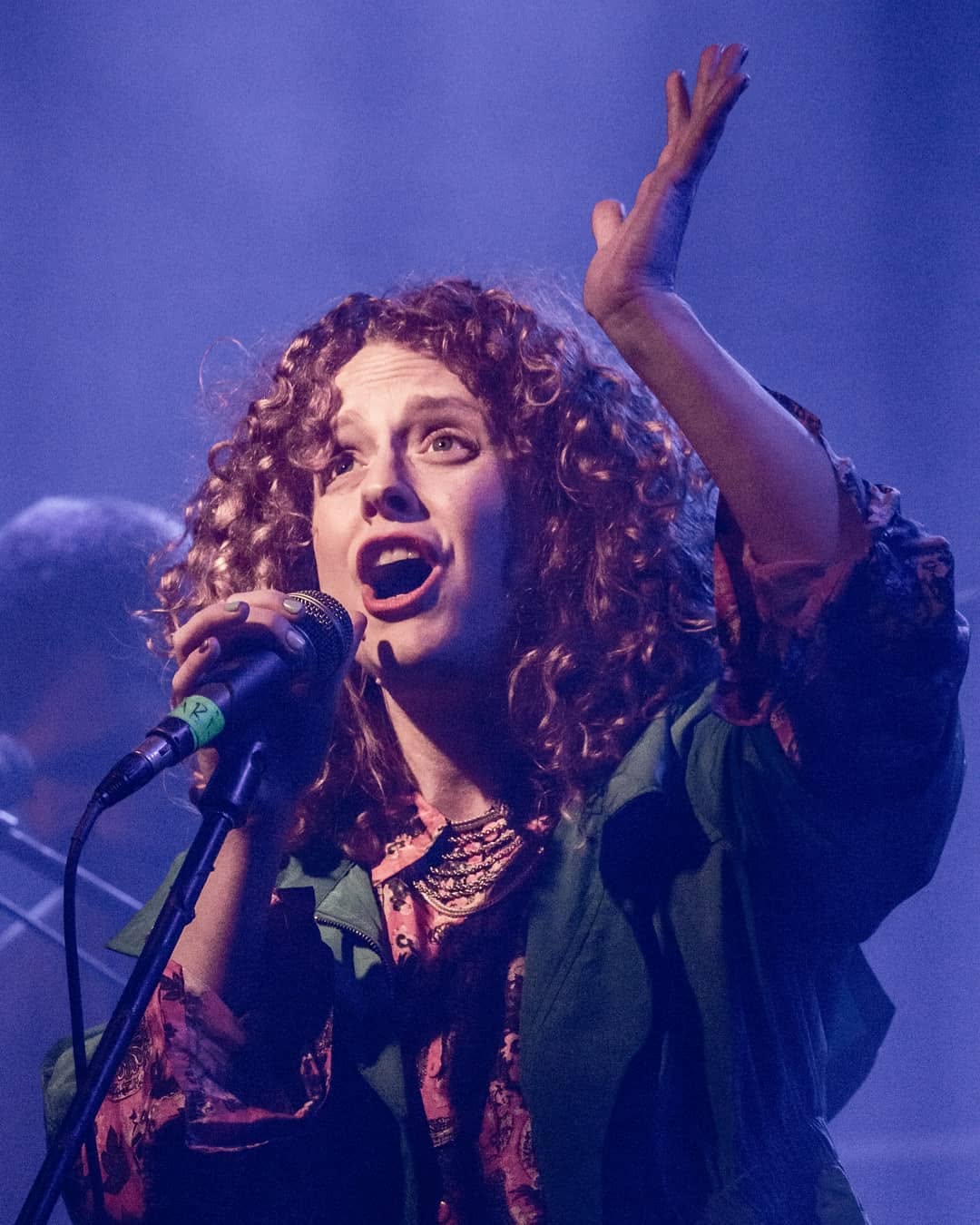 Noa Lembersky singing with one hand raised under violet stage lights